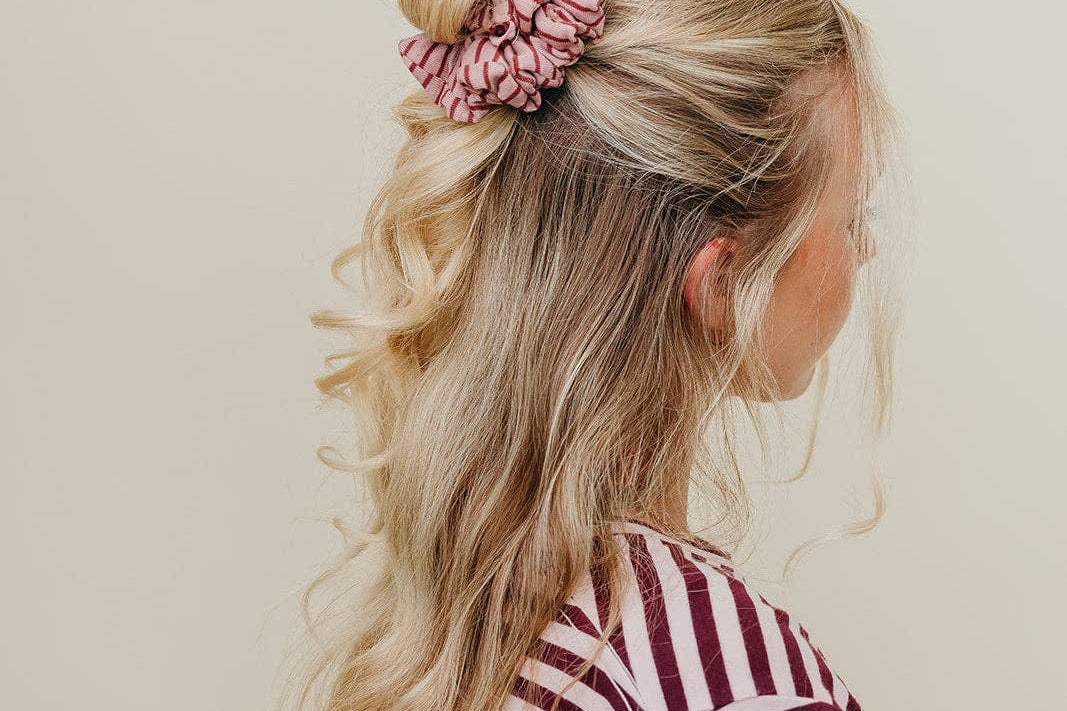 Woman with styled hair and a pink scrunchie against a neutral background