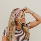 Woman wearing a striped shirt and pink headband against a beige background