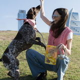 Woman playing with a dog in an open field with buildings in the background