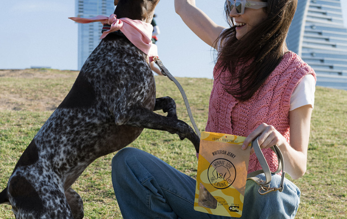 Woman playing with a dog in an open field with buildings in the background