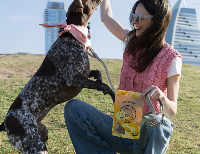 Woman playing with a dog in an open field with buildings in the background