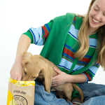 Woman holding a puppy next to a bag of dog treats on a white background