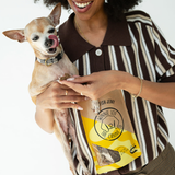 Woman holding a small dog and a bag of treats with a brand logo.