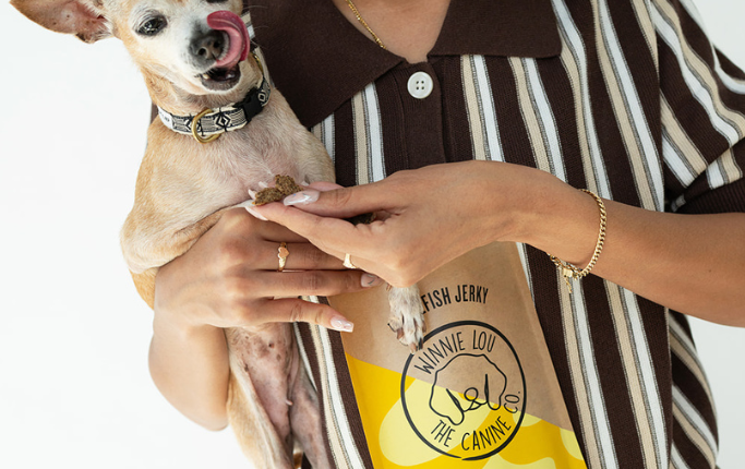 Woman holding a small dog and a bag of treats with a brand logo.