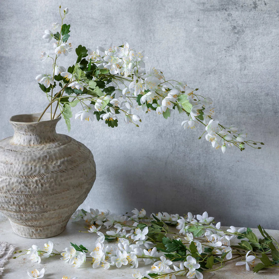 Abigail Ahern Artificial Cream Campanula stems arranged in a textured stone vase with loose blossoms on the table