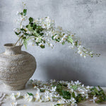 Abigail Ahern Artificial Cream Campanula stems arranged in a textured stone vase with loose blossoms on the table