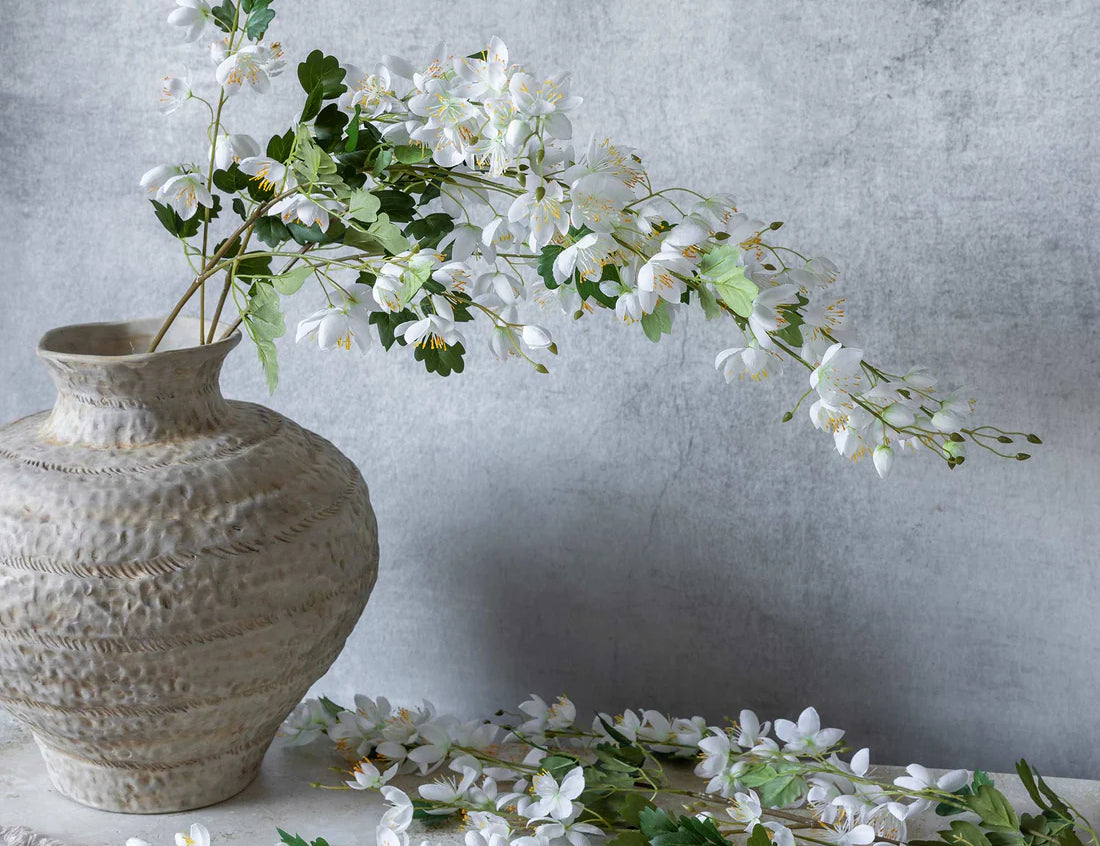 Abigail Ahern Artificial Cream Campanula stems arranged in a textured stone vase with loose blossoms on the table