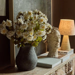 Abigail Ahern Artificial Dahlia Evening Dew stems arranged in a dark vase on a console with a lamp and books