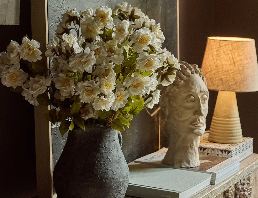 Abigail Ahern Artificial Dahlia Evening Dew stems arranged in a dark vase on a console with a lamp and books