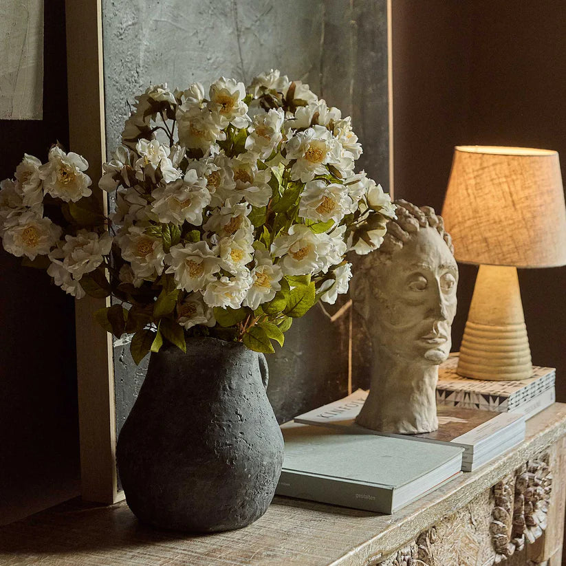 Abigail Ahern Artificial Dahlia Evening Dew stems arranged in a dark vase on a console with a lamp and books