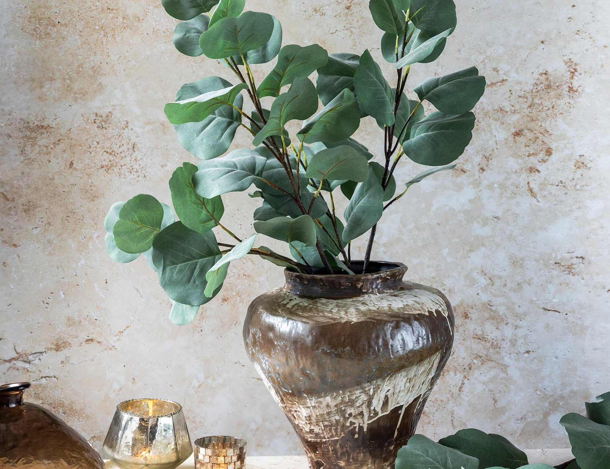 Abigail Ahern Artificial Eucalyptus Silver Dollar stems in a bronze vase on a table with candles