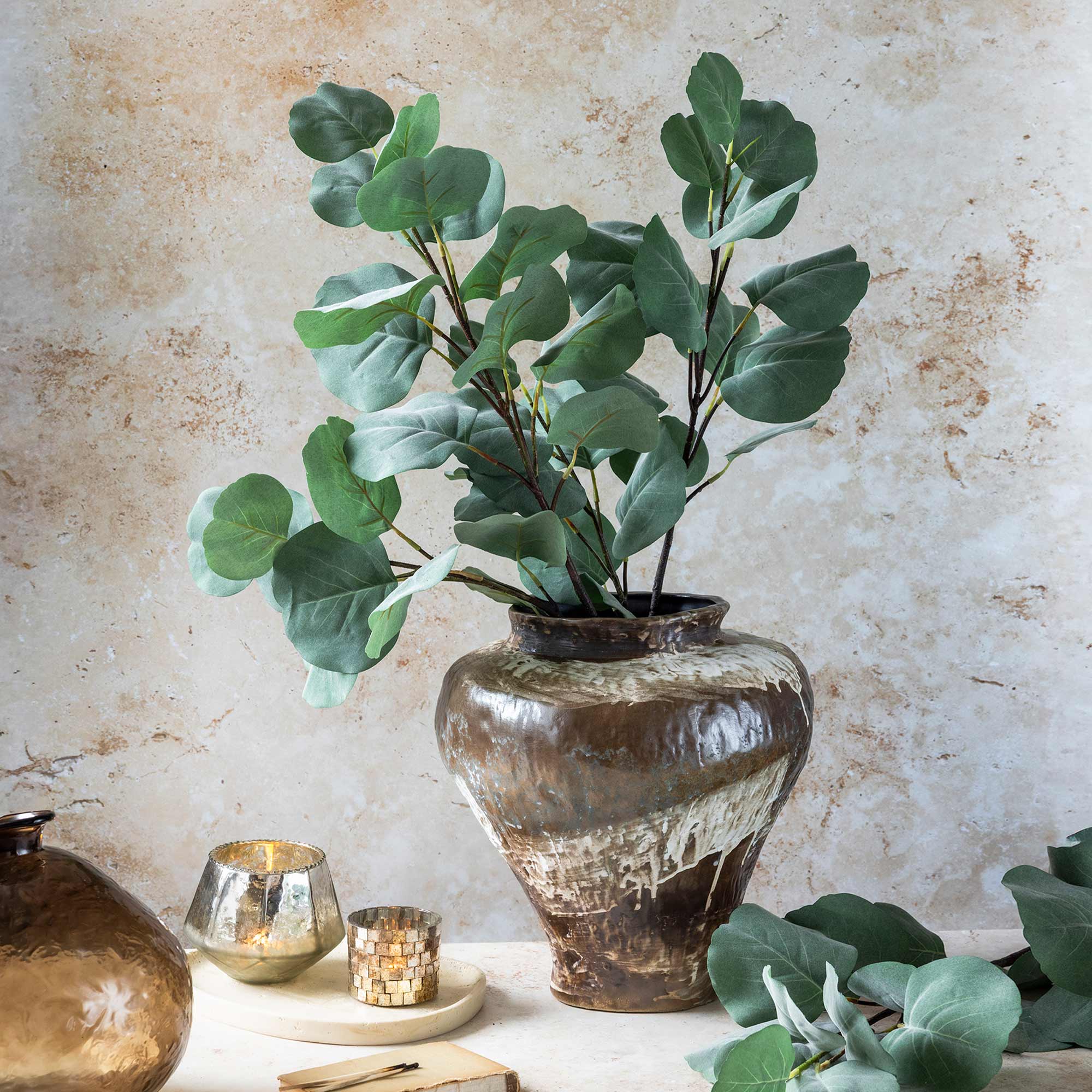 Abigail Ahern Artificial Eucalyptus Silver Dollar stems in a bronze vase on a table with candles