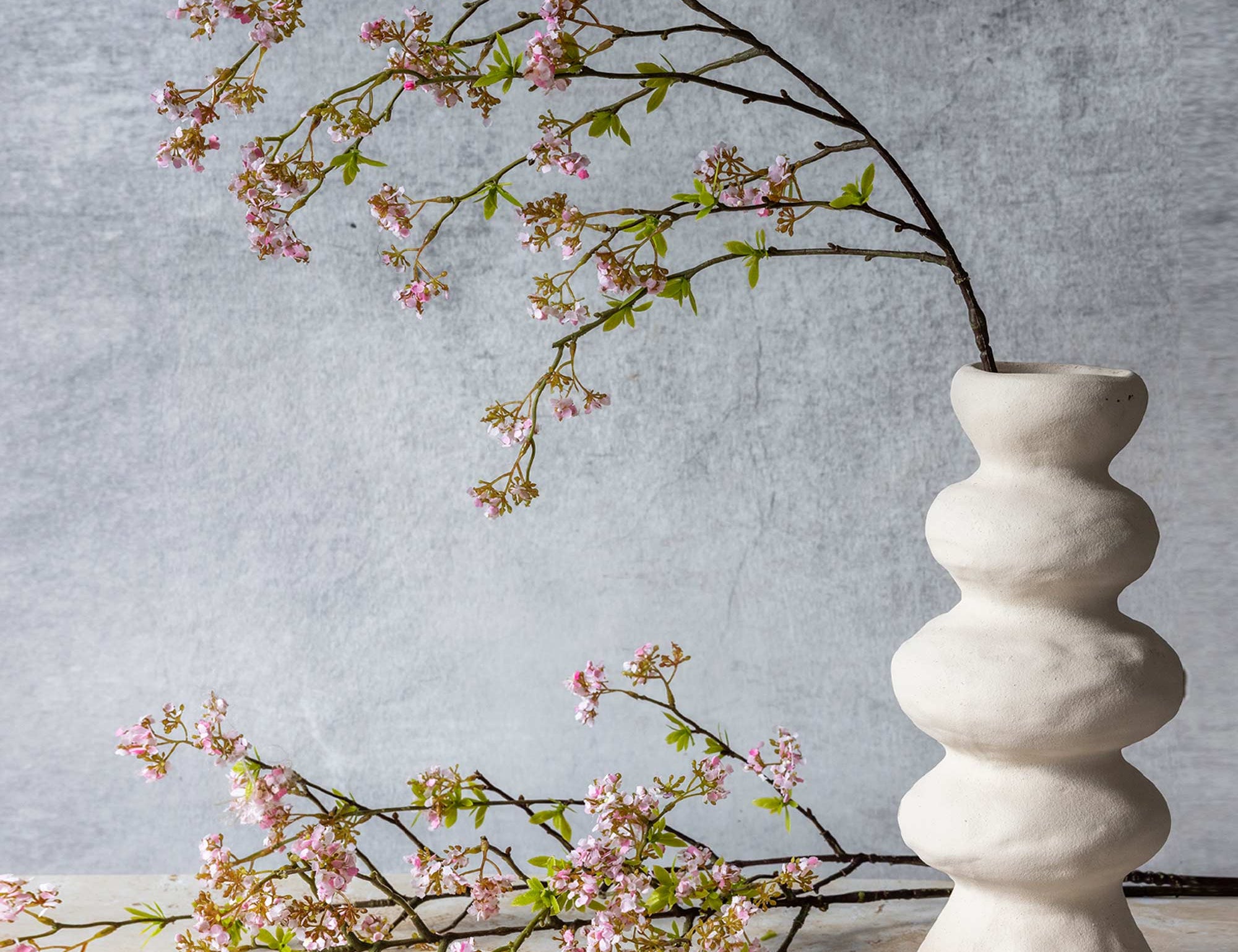 Abigail Ahern Artificial Pink Cherry Blossom branch arching from a white sculptural vase