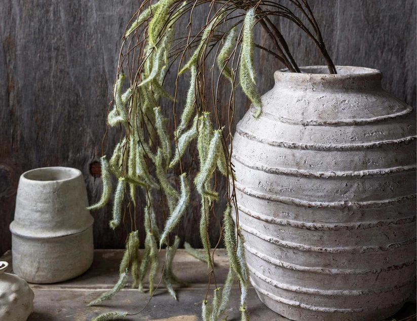 Abigail Ahern Artificial Trailing Catkin stems draping from a white ribbed vase on a dark shelf