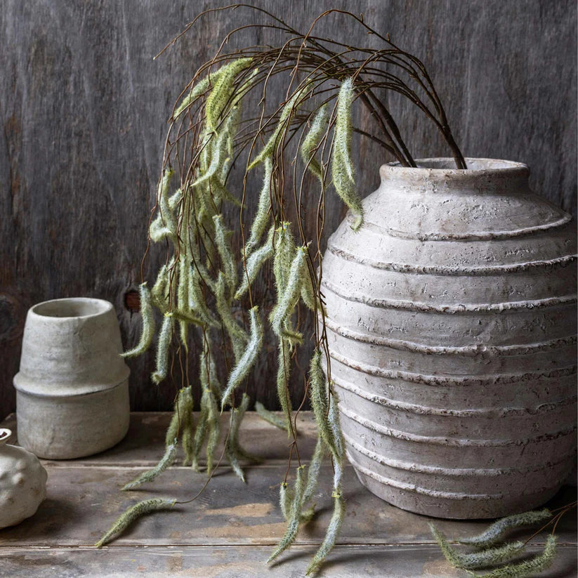 Abigail Ahern Artificial Trailing Catkin stems draping from a white ribbed vase on a dark shelf