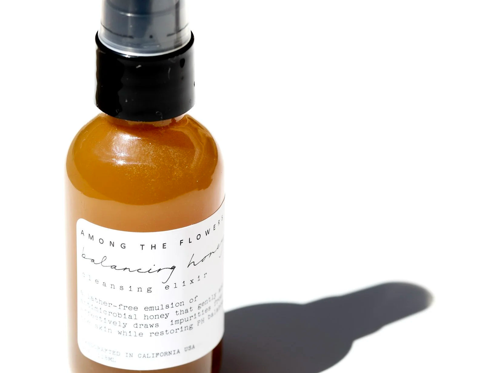 Among the Flowers Balancing Honey Cleanser, close-up of the amber pump bottle casting a shadow