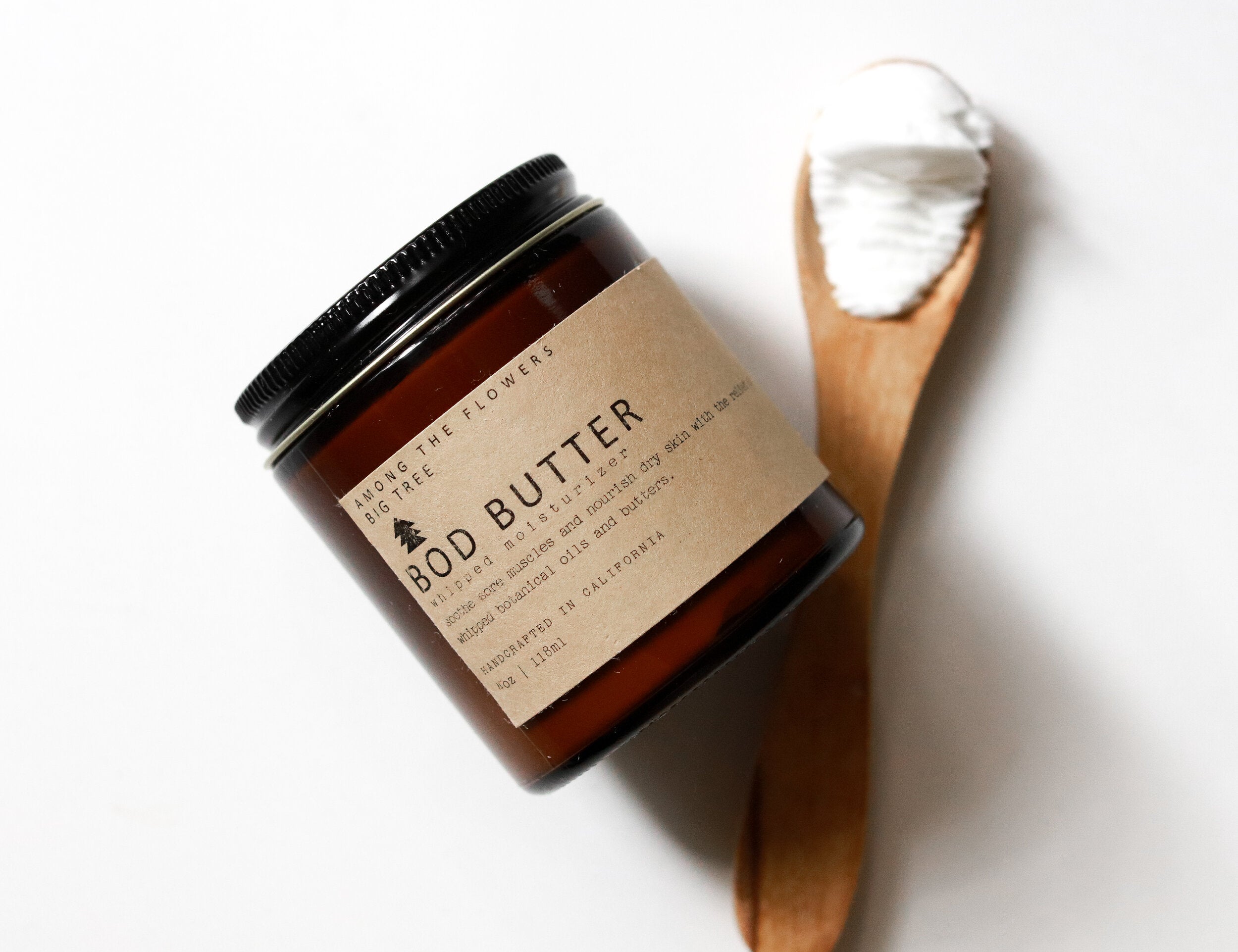 Among the Flowers Big Tree Bod Butter in an amber glass jar with a wooden spoon of whipped butter