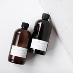 Two amber pump bottles of Among the Flowers Botanical Aloe 8oz Lotion lying on a white surface