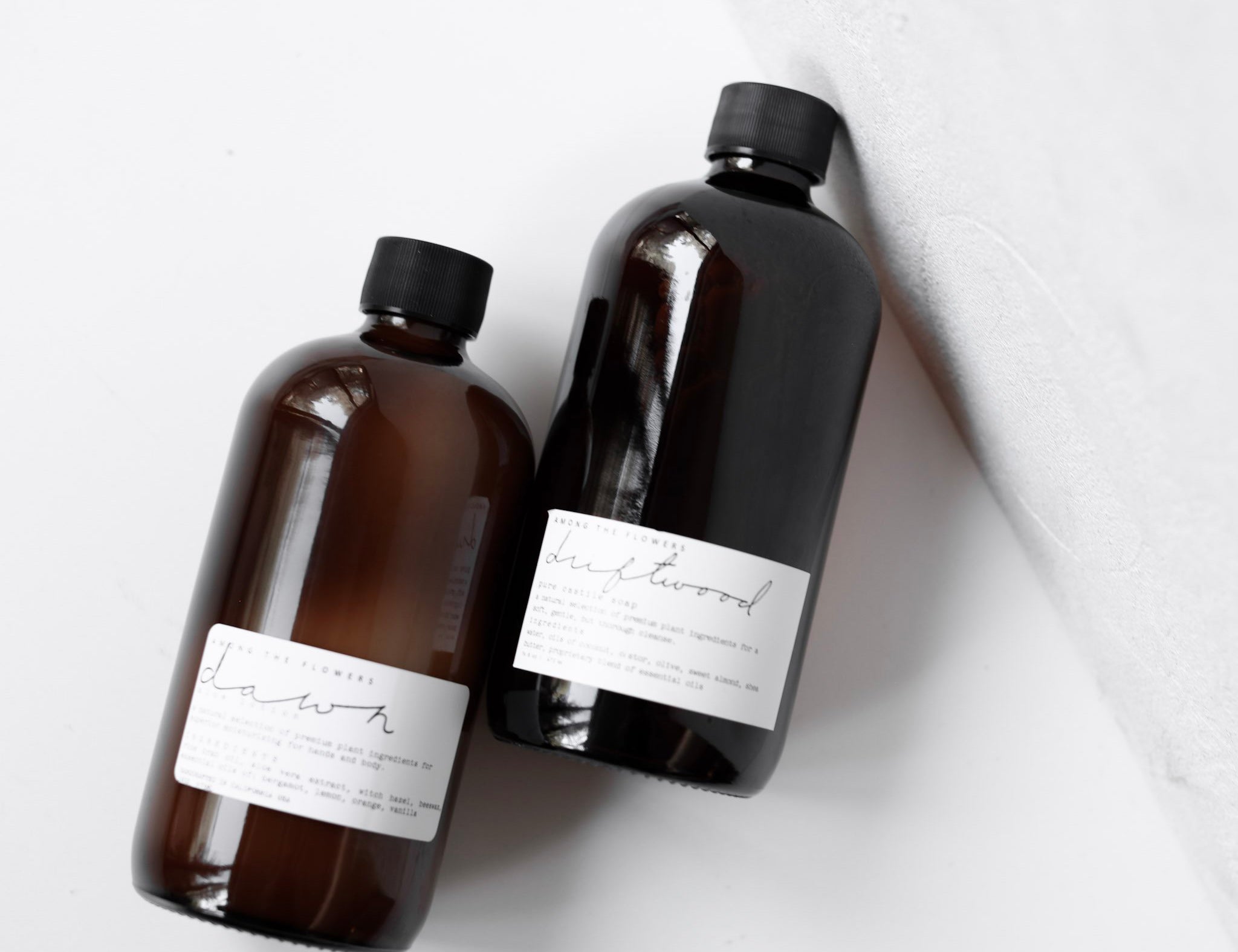 Two amber pump bottles of Among the Flowers Botanical Aloe 8oz Lotion lying on a white surface