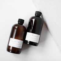 Two amber pump bottles of Among the Flowers Botanical Aloe 8oz Lotion lying on a white surface