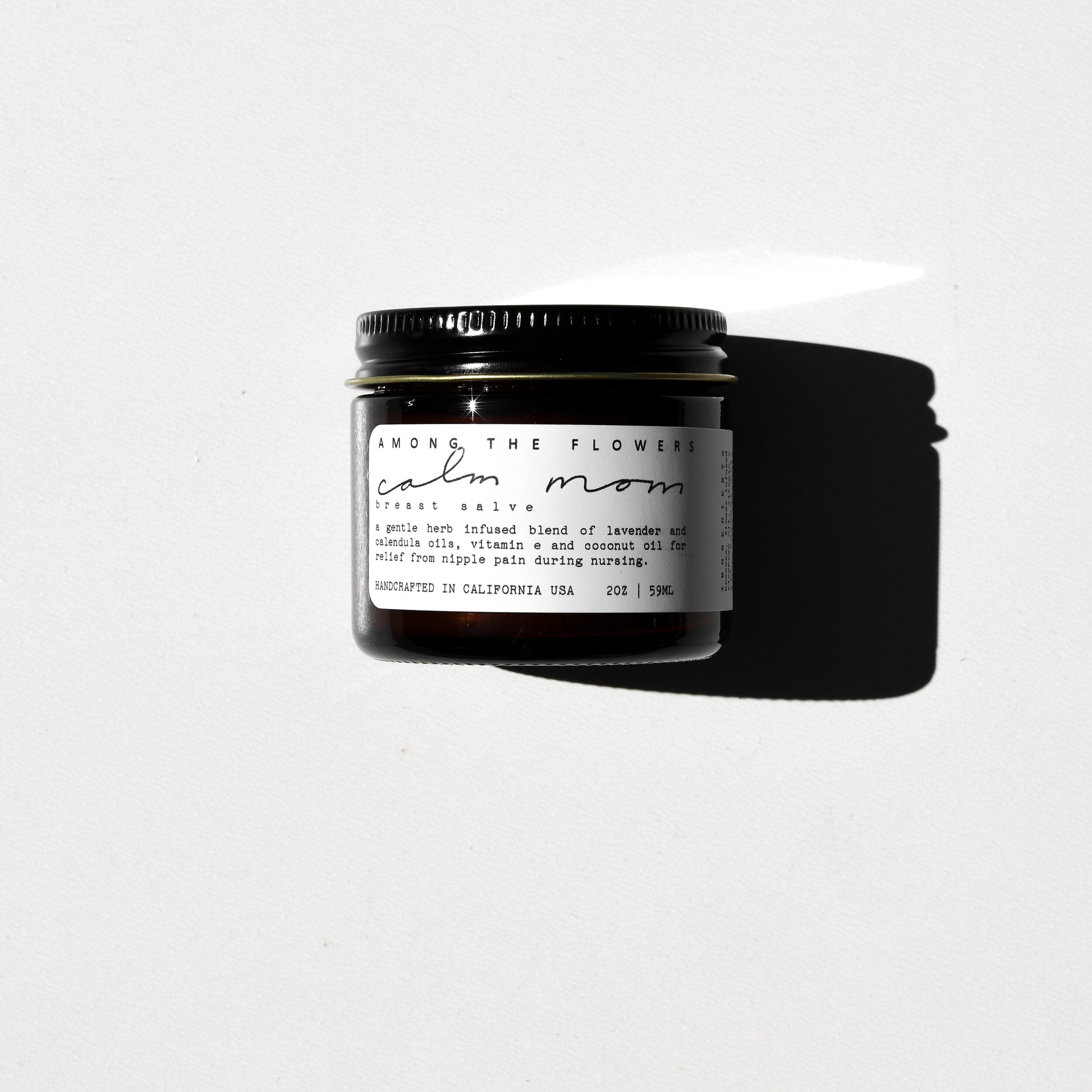 Among the Flowers Calm Mom Breast Salve in a small amber glass jar with a black lid