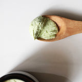 Wooden spoon holding a scoop of pale green Among the Flowers Calming Baby Balm