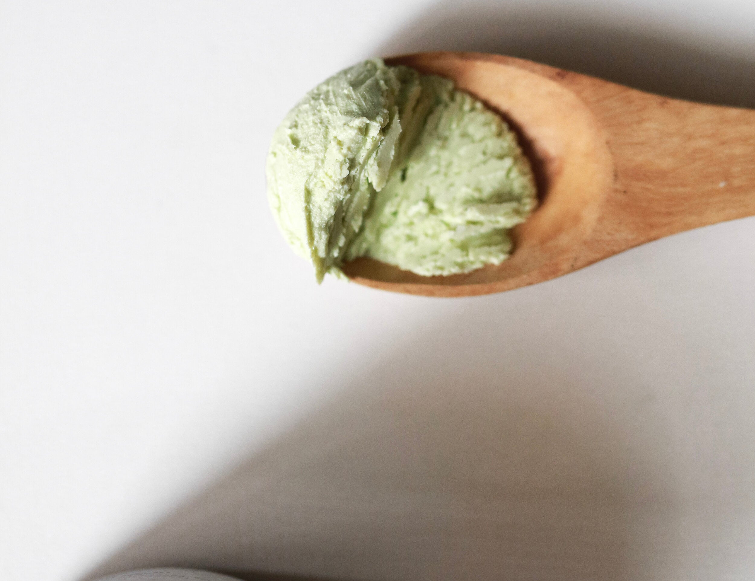 Wooden spoon holding a scoop of pale green Among the Flowers Calming Baby Balm