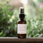 Among the Flowers Camp Mist Insect Shield amber spray bottle on a ledge with greenery behind