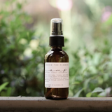 Among the Flowers Camp Mist Insect Shield amber spray bottle on a ledge with greenery behind