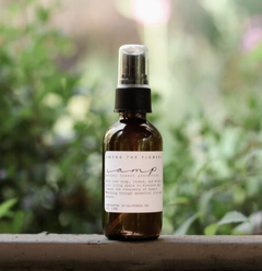 Among the Flowers Camp Mist Insect Shield amber spray bottle on a ledge with greenery behind
