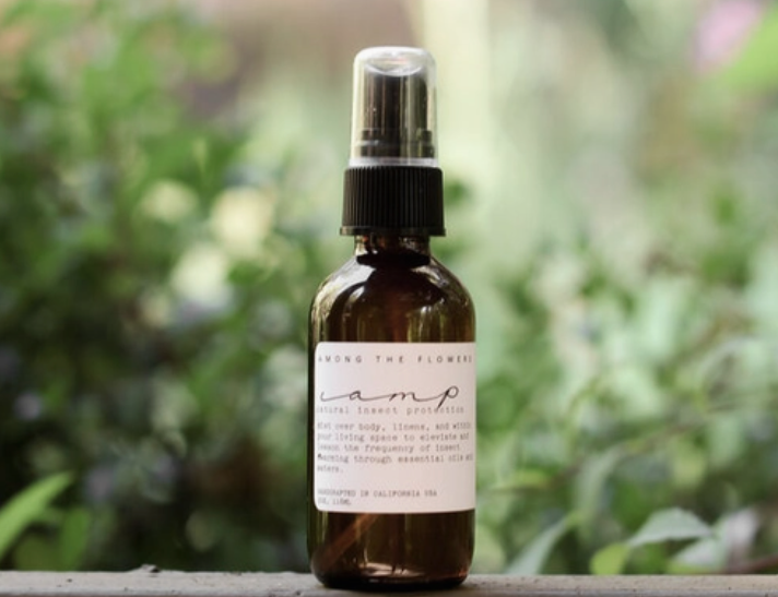 Among the Flowers Camp Mist Insect Shield amber spray bottle on a ledge with greenery behind