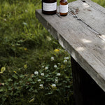 Among the Flowers Camp Mist Insect Shield bottle on the edge of a wooden picnic table in a green meadow
