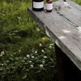 Among the Flowers Camp Mist Insect Shield bottle on the edge of a wooden picnic table in a green meadow