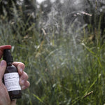 Hand spraying the Among the Flowers Camp Mist Insect Shield in a grassy meadow
