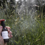 Hand spraying the Among the Flowers Camp Mist Insect Shield in a grassy meadow