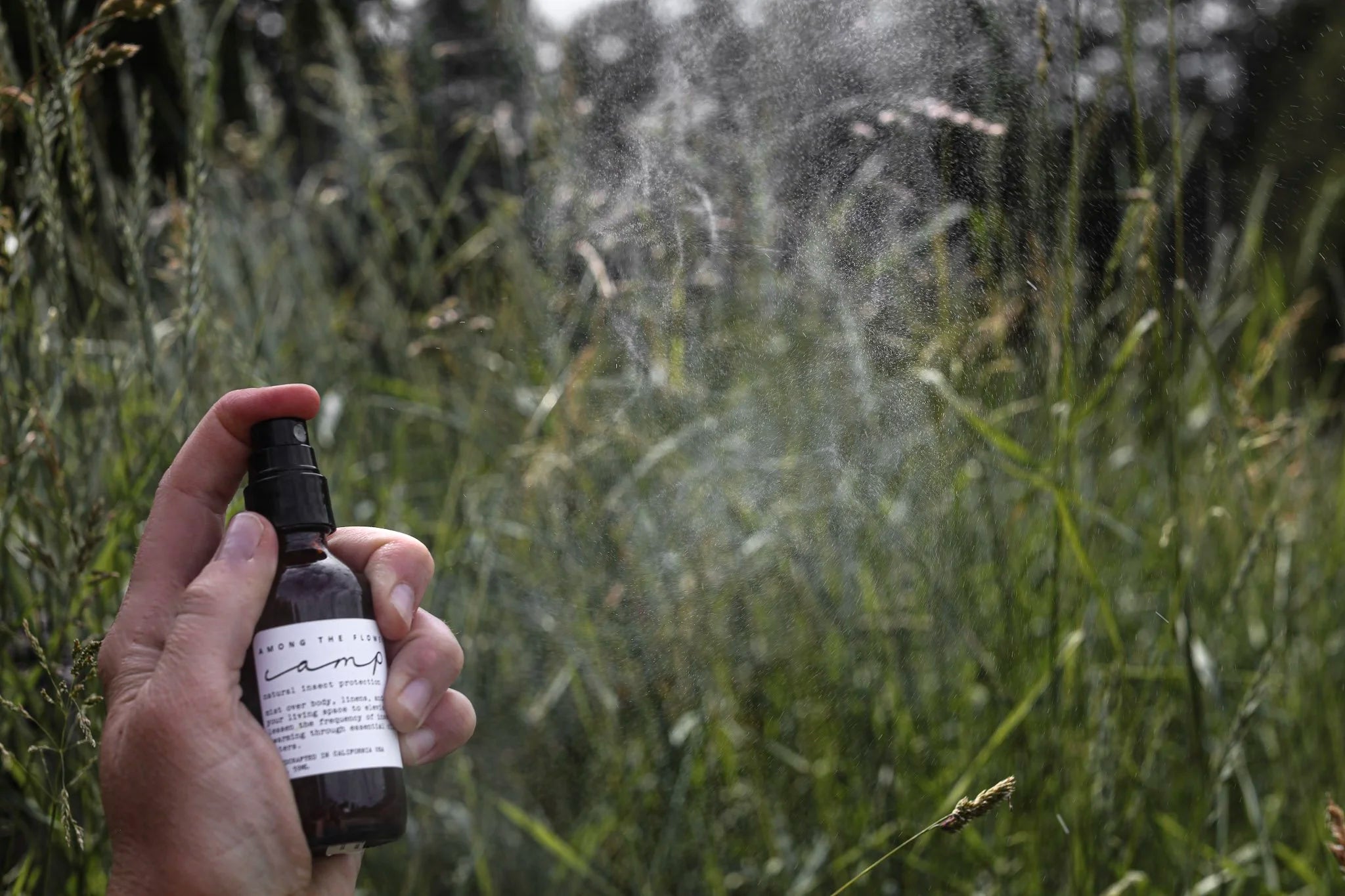 Hand spraying the Among the Flowers Camp Mist Insect Shield in a grassy meadow