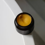 Among the Flowers Gold Balancing Face Balm open black jar showing the golden balm