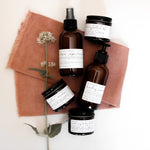 Among the Flowers Lavender Lullaby Baby Wash with other amber-bottle baby products on a rust linen cloth