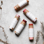 Among the Flowers Lip and Cheek Tint tubes scattered on a stone surface with dried botanicals