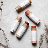 Among the Flowers Lip and Cheek Tint tubes scattered on a stone surface with dried botanicals