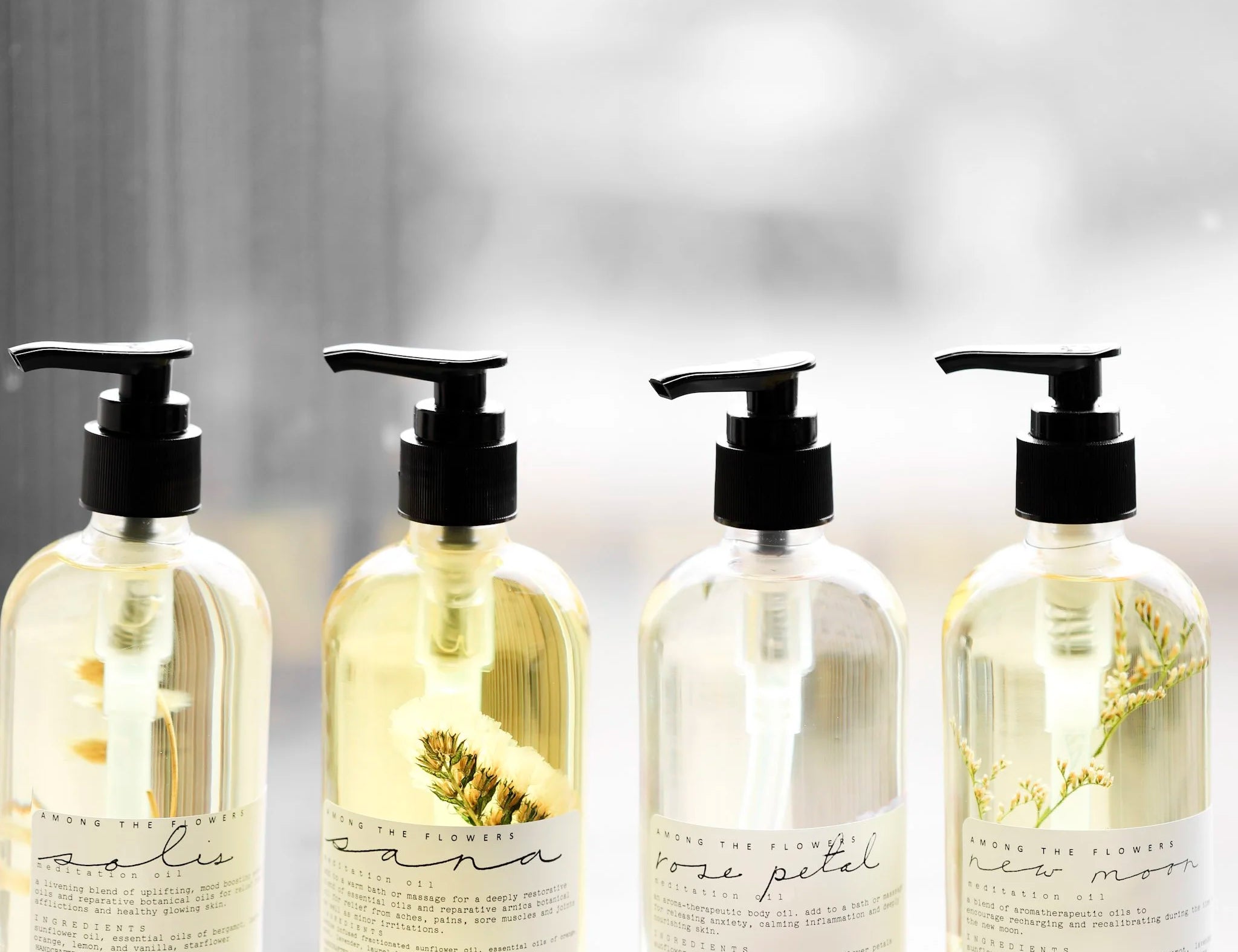 Among the Flowers Meditation Oils in four scents lined up in clear pump bottles by a window