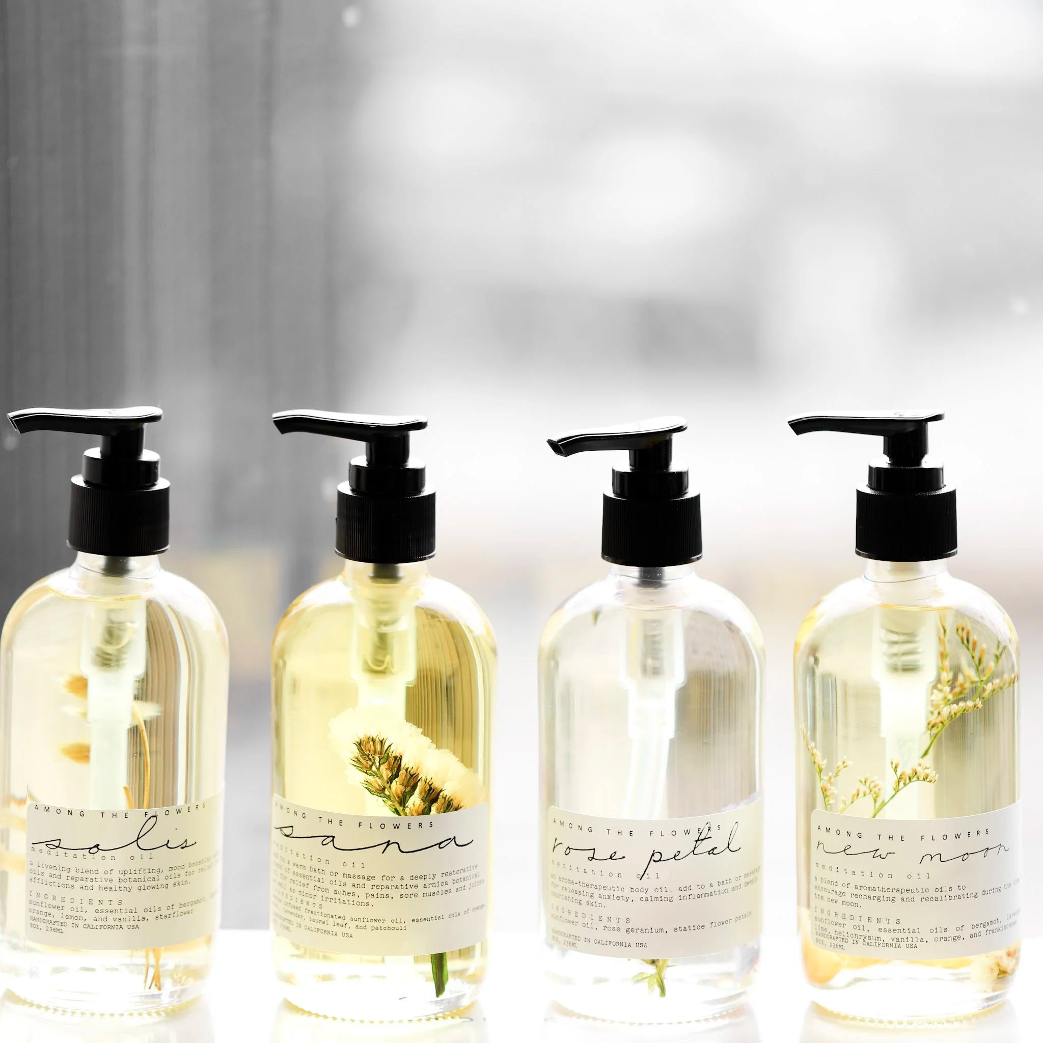 Among the Flowers Meditation Oils in four scents lined up in clear pump bottles by a window