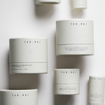 Among the Flowers Tallow Body Cream jars in white cylinder packaging scattered from above