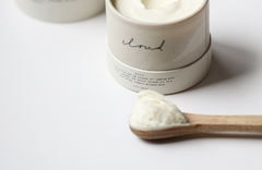 Among the Flowers Tallow Body Cream in an open white jar with a wooden spoon of cream