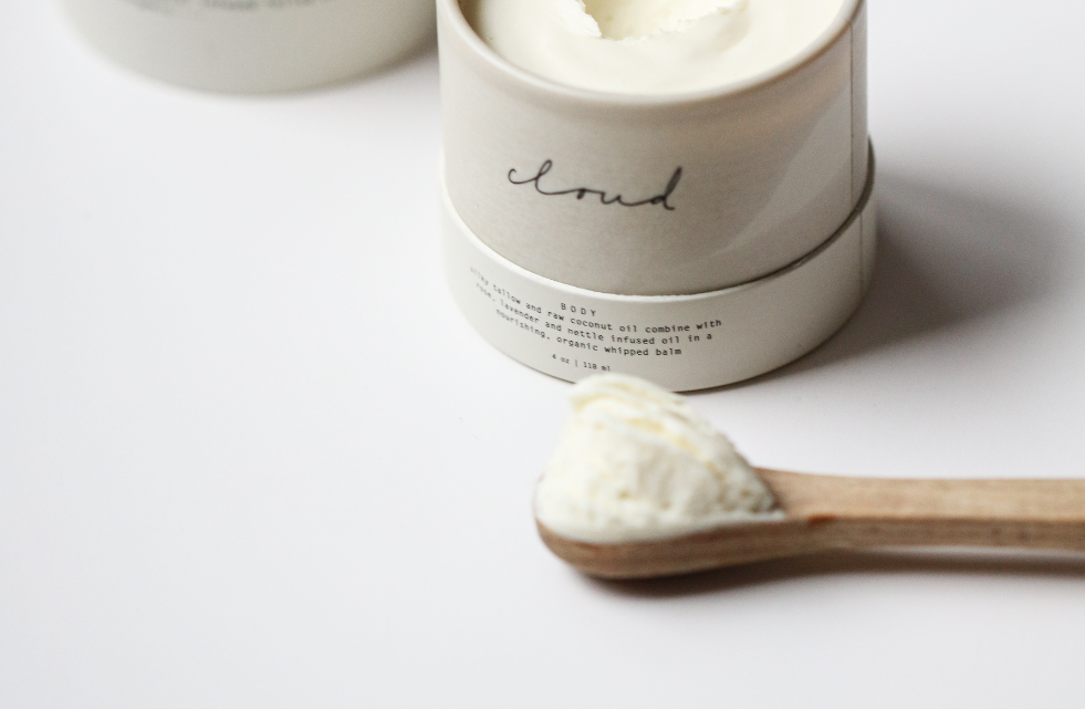Among the Flowers Tallow Body Cream in an open white jar with a wooden spoon of cream