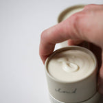 Hand lifting the lid off an Among the Flowers Tallow Body Cream jar showing the whipped cream