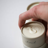 Hand lifting the lid off an Among the Flowers Tallow Body Cream jar showing the whipped cream