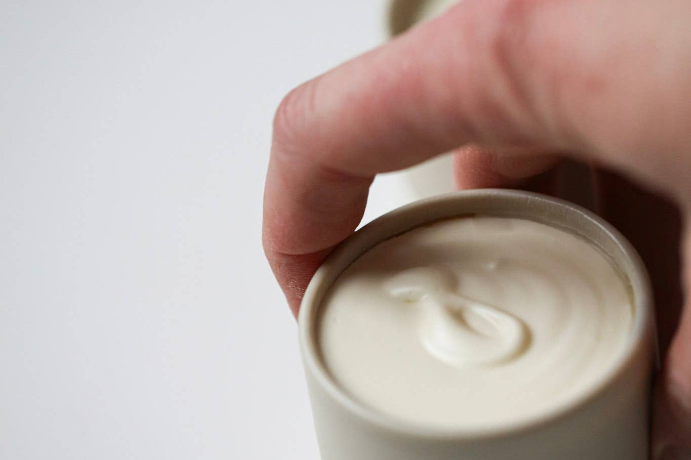 Hand lifting the lid off an Among the Flowers Tallow Body Cream jar showing the whipped cream