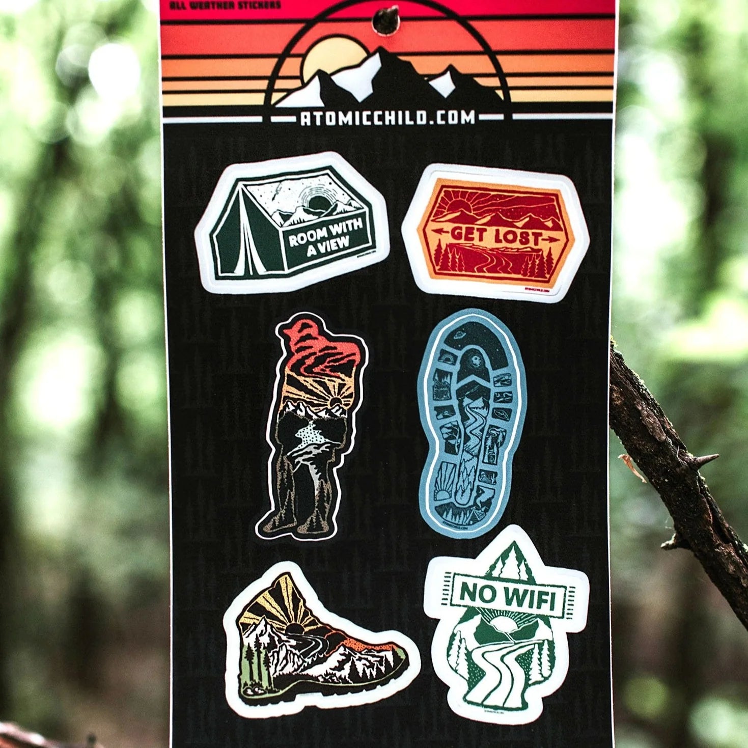 Atomicchild Hiking Mini Sticker Sheet held up against a forest background