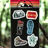 Atomicchild Hiking Mini Sticker Sheet held up against a forest background